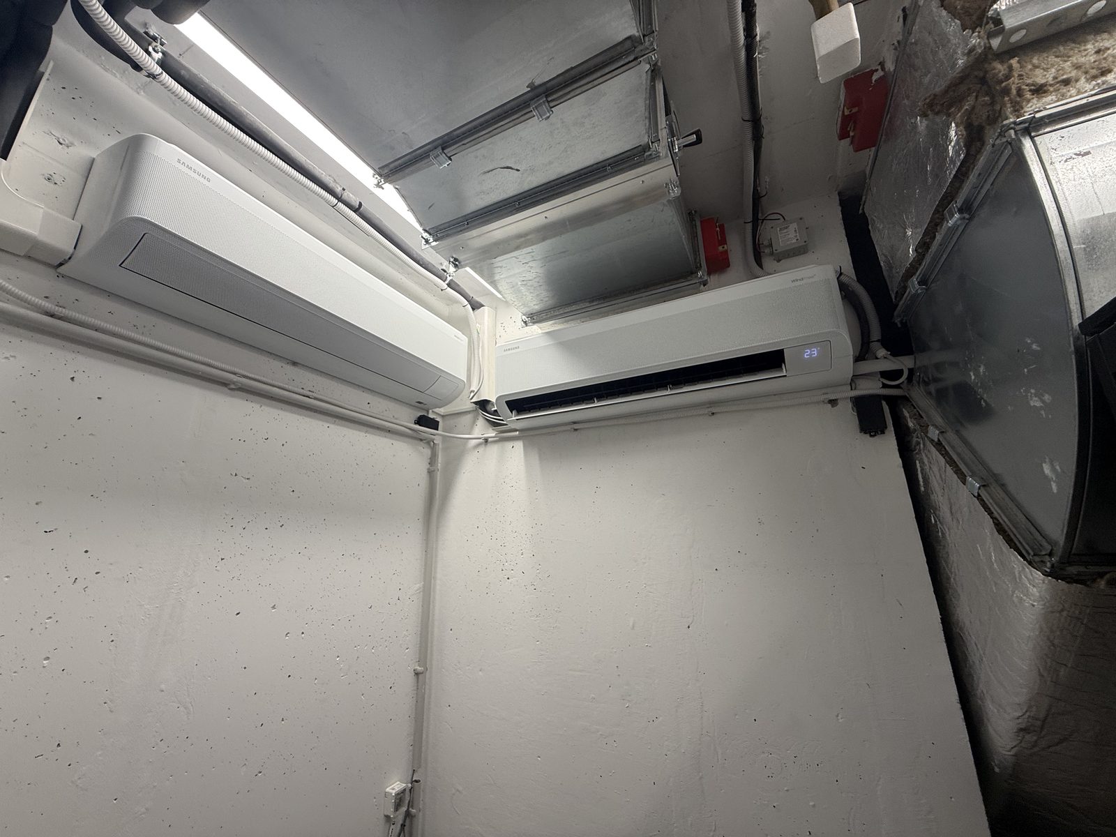 Két klíma beltéri egység egy gépészeti helyiség falán, légtechnikai vezetékek mellett